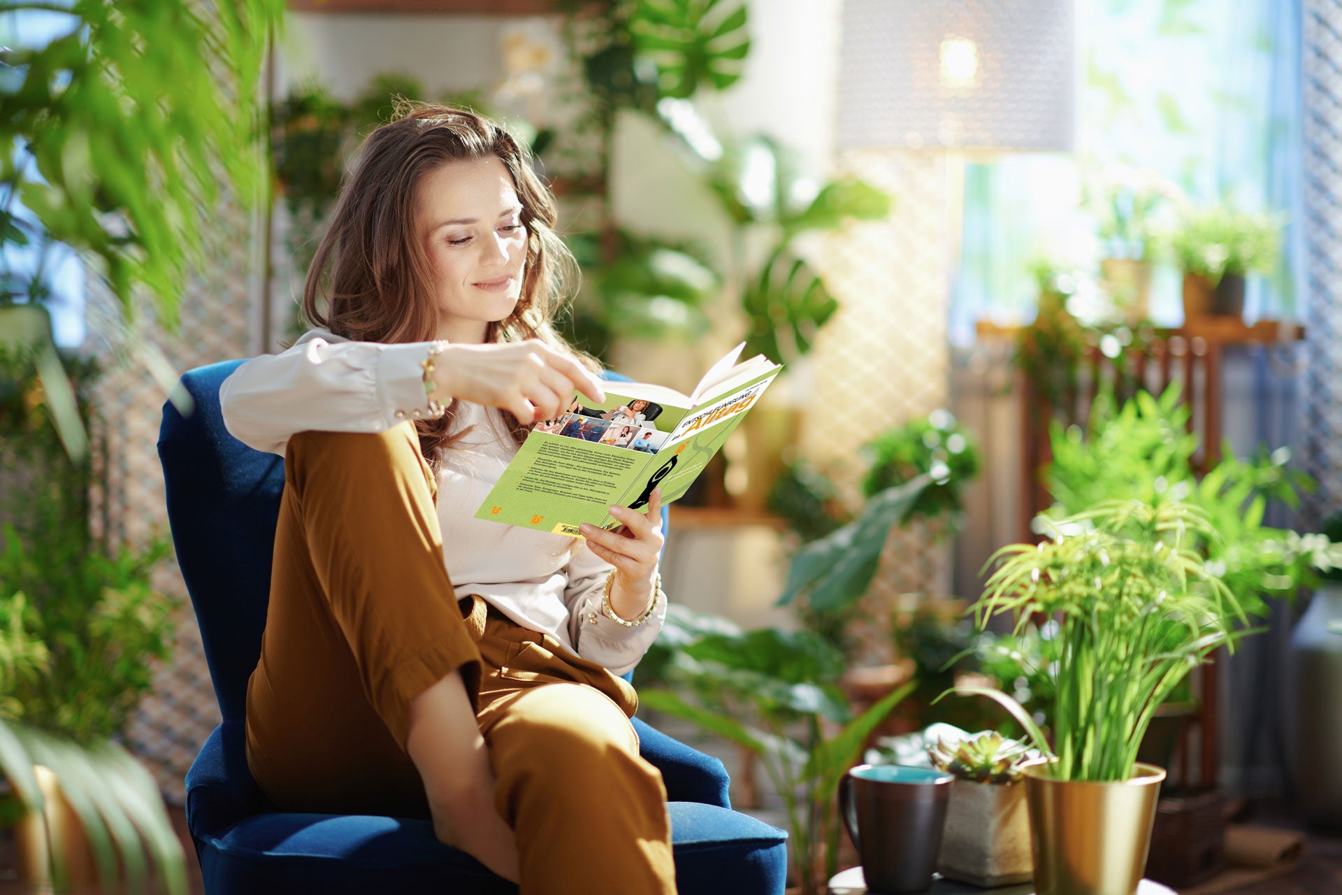 Frau sitzt mit einem Buch auf einem Balkon mit vielen Pflanzen und liest Kategorie „Freizeit“ EDITION XXL